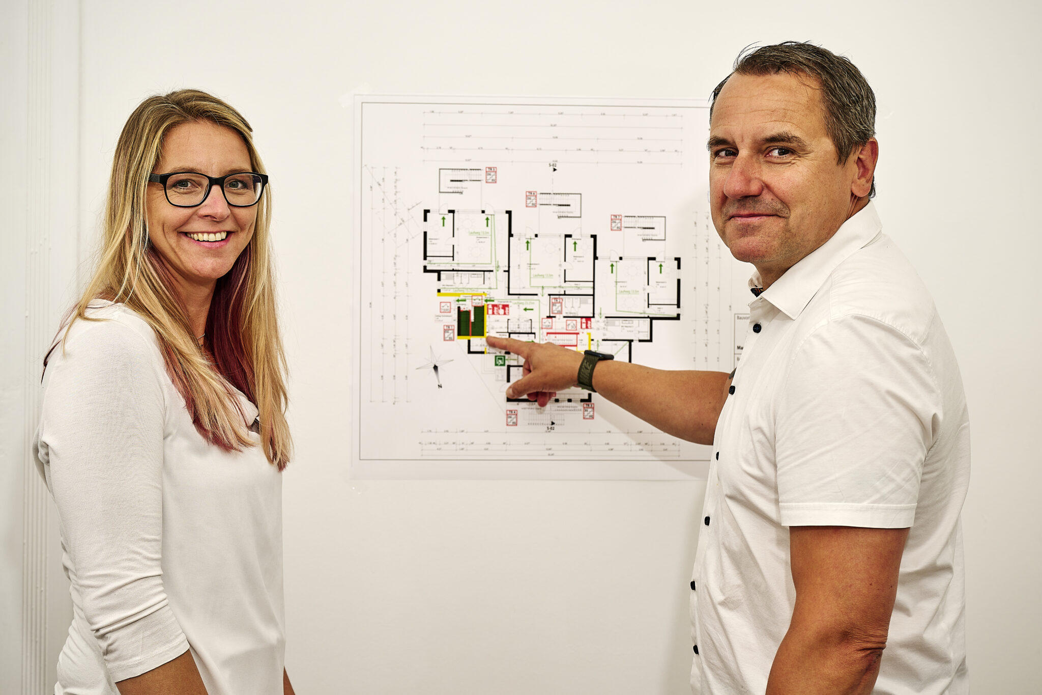 Zwei Mitarbeitende der GfB besprechen im Düsseldorfer Büro einen Feuerwehrplan an der Wand
